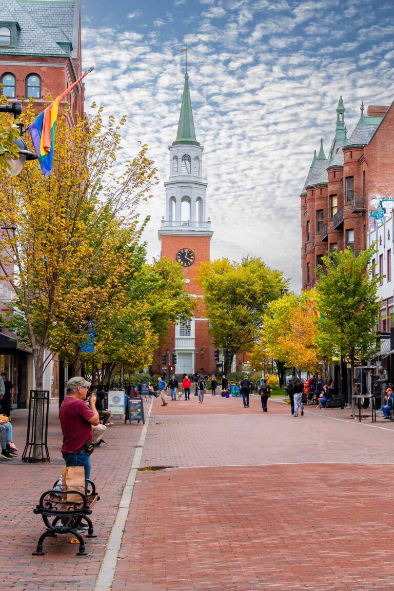 A view of Church Street Marketplace in Burlington, Vermont with people walking along the brick-paved pedestrian street. Trees with fall colors line the walkway.