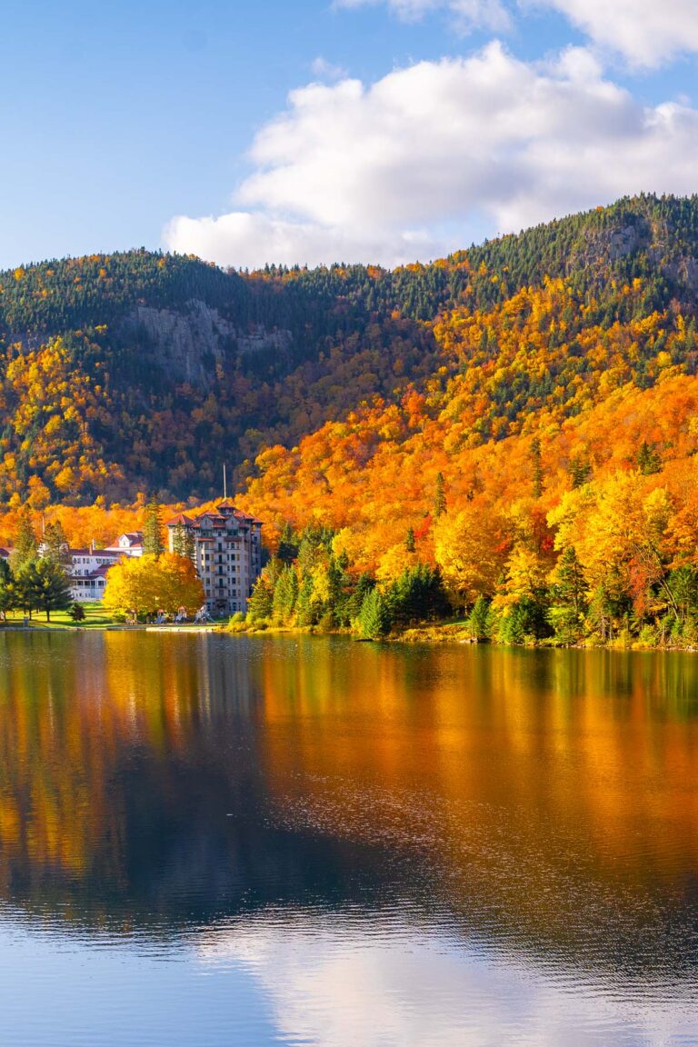Lake Gloriette in Dixville Notch, New Hampshire reflecting colorful fall trees and a hotel with forested hills in the background.