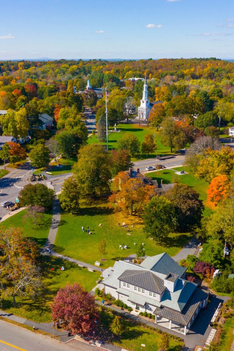 Aerial view of Lexington Green during fall, with colorful trees, historic buildings, and a white steepled church lining the edges of the common.