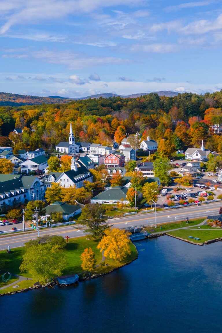 Aerial view of Meredith at Lake Winnipesaukee, New Hampshire with colorful fall trees, white church steeples, and waterfront homes.