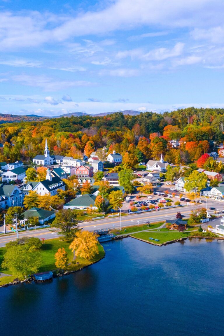 Aerial view of Meredith at Lake Winnipesaukee, New Hampshire with colorful fall trees, white church steeples, and waterfront homes.