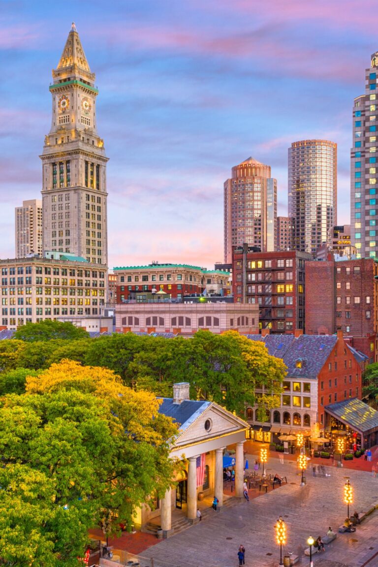 A sunset view of Quincy Market and Faneuil Hall with the Boston skyline in the background. 