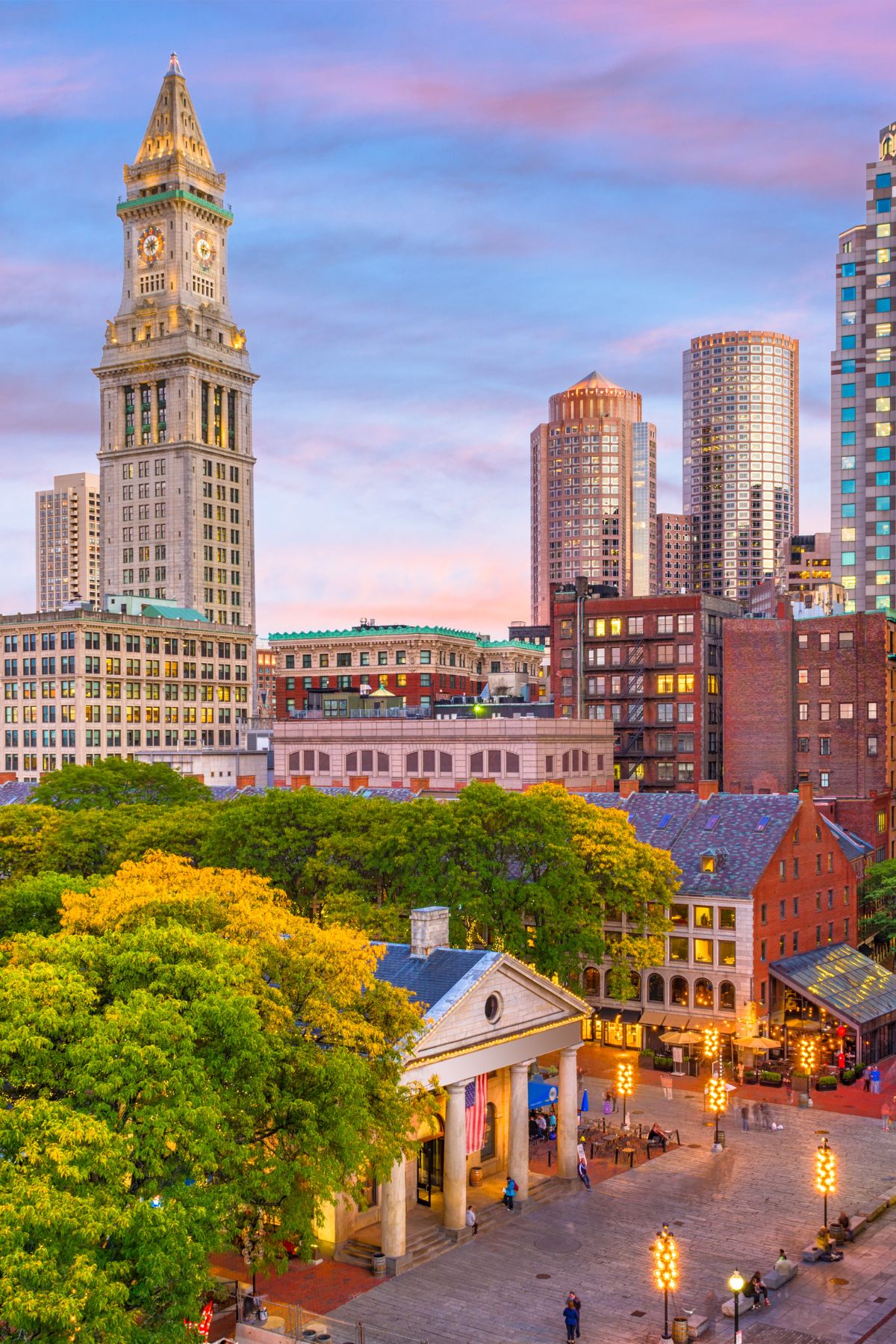 A sunset view of Quincy Market and Faneuil Hall with the Boston skyline in the background. 