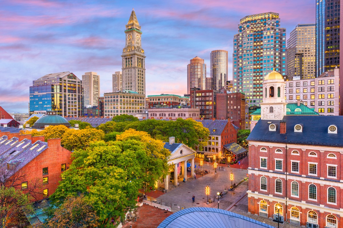 A sunset view of Quincy Market and Faneuil Hall with the Boston skyline in the background. 