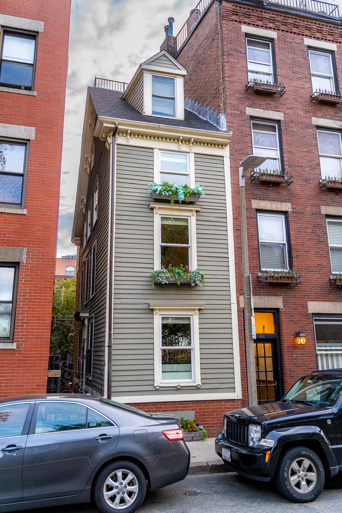 A narrow olive-green house with flower boxes known as the Skinny House squeezed tightly between two brick buildings in the North End of Boston.