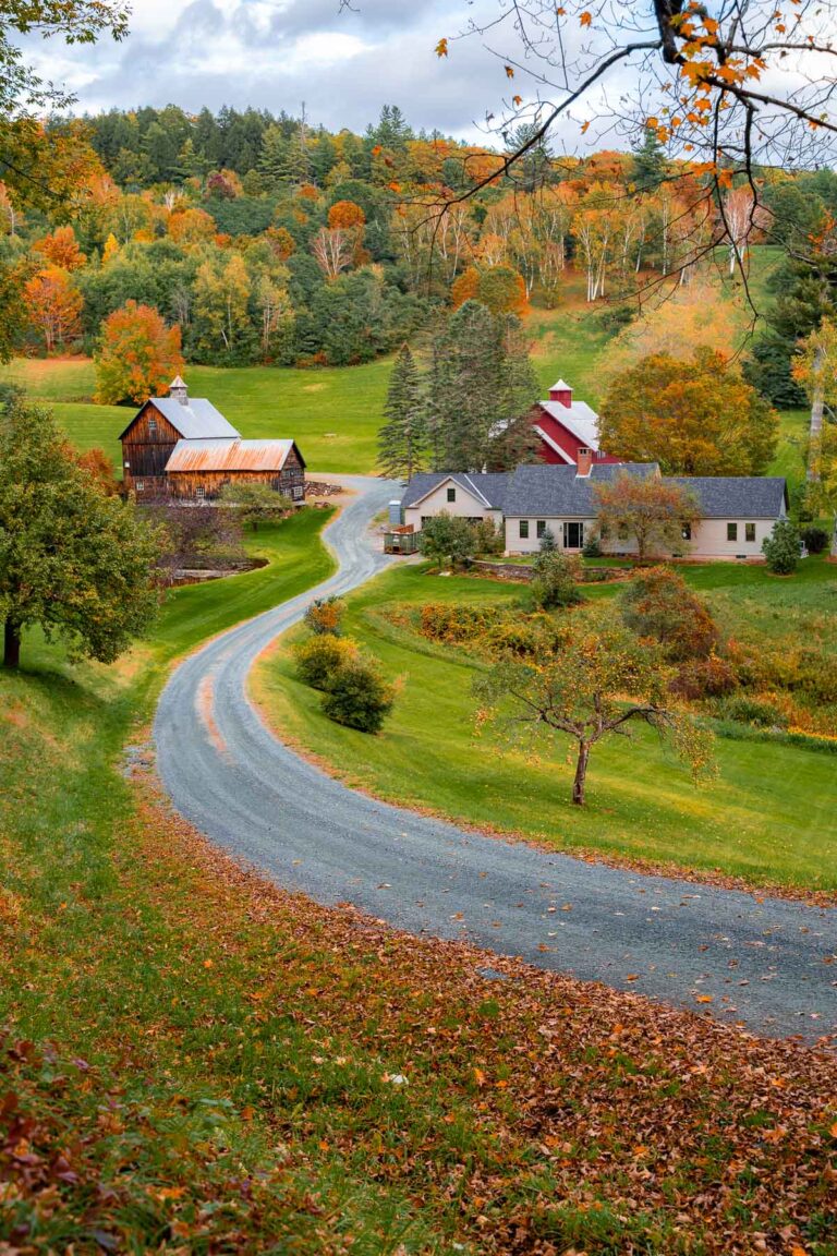 A winding dirt road leads to Sleepy Hollow Farm in Woodstock, Vermont, with colorful fall foliage covering the surrounding hills and trees.