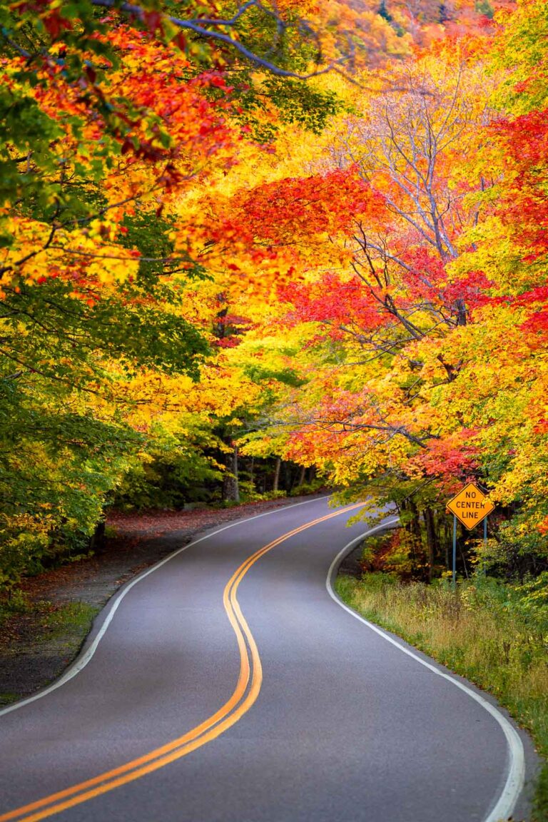 A winding road at Smuggler’s Notch, one of the best scenic drives in Vermont, surrounded by vibrant fall foliage in shades of red, orange, and yellow.