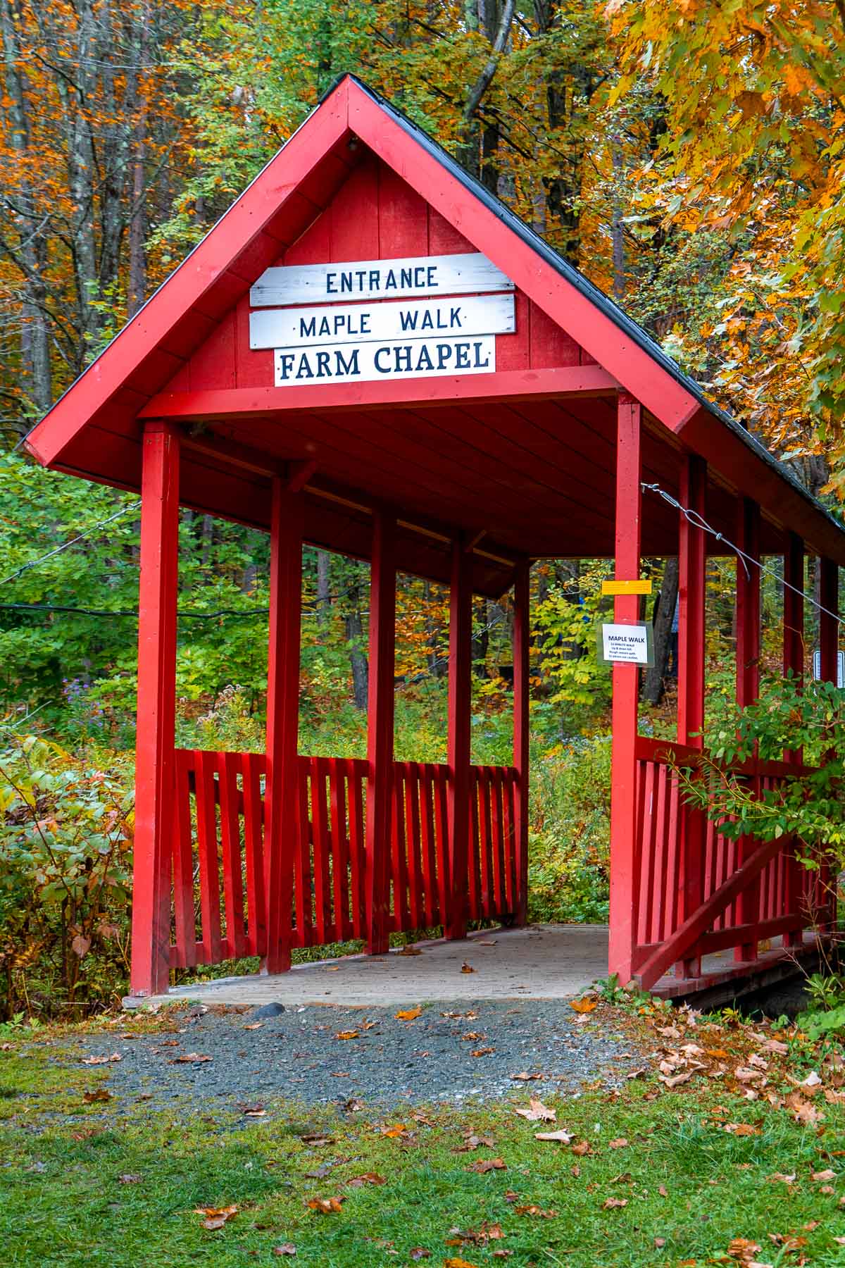 A small red covered bridge marks the entrance to the Maple Walk and Farm Chapel at Sugarbush Farm in Vermont, surrounded by bright fall leaves.