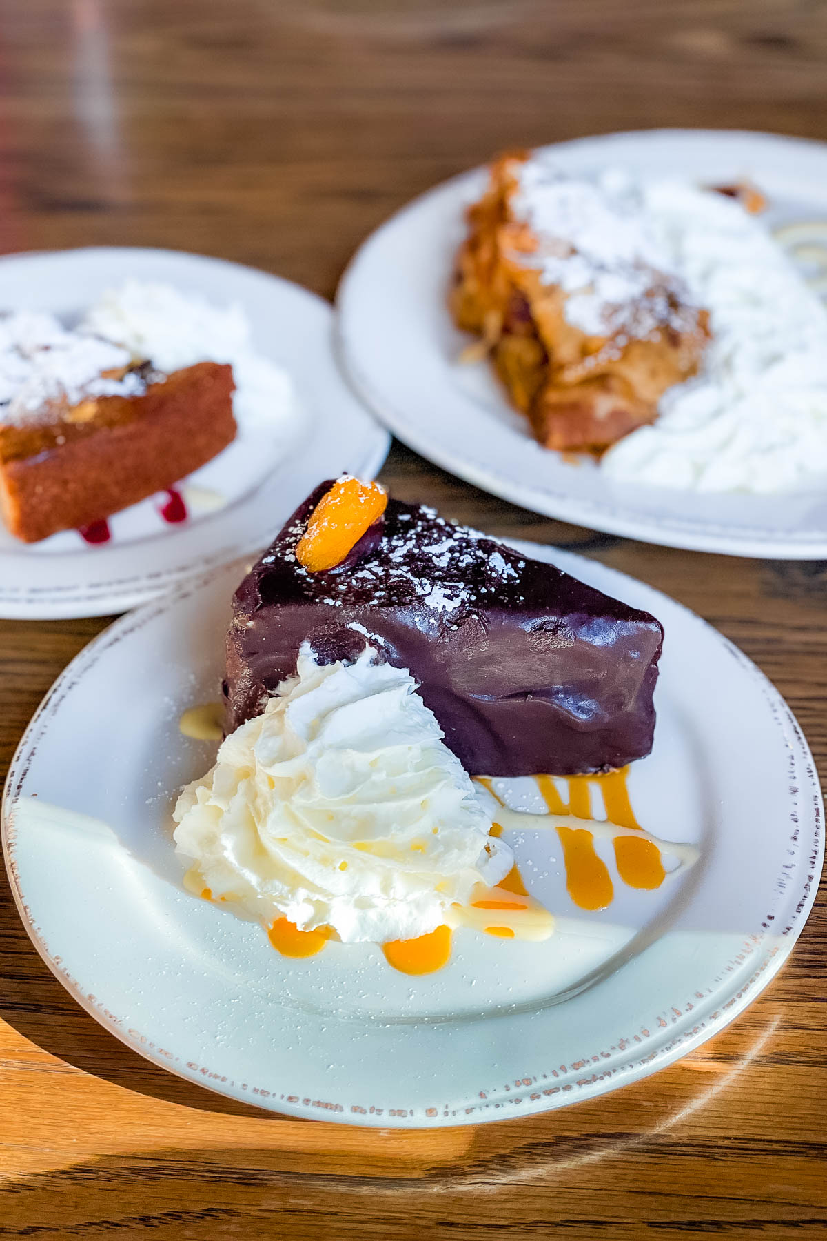 Close-up of dessert plates from Trapp Family Lodge in Vermont, featuring a chocolate-covered cake slice topped with whipped cream and caramel drizzle.