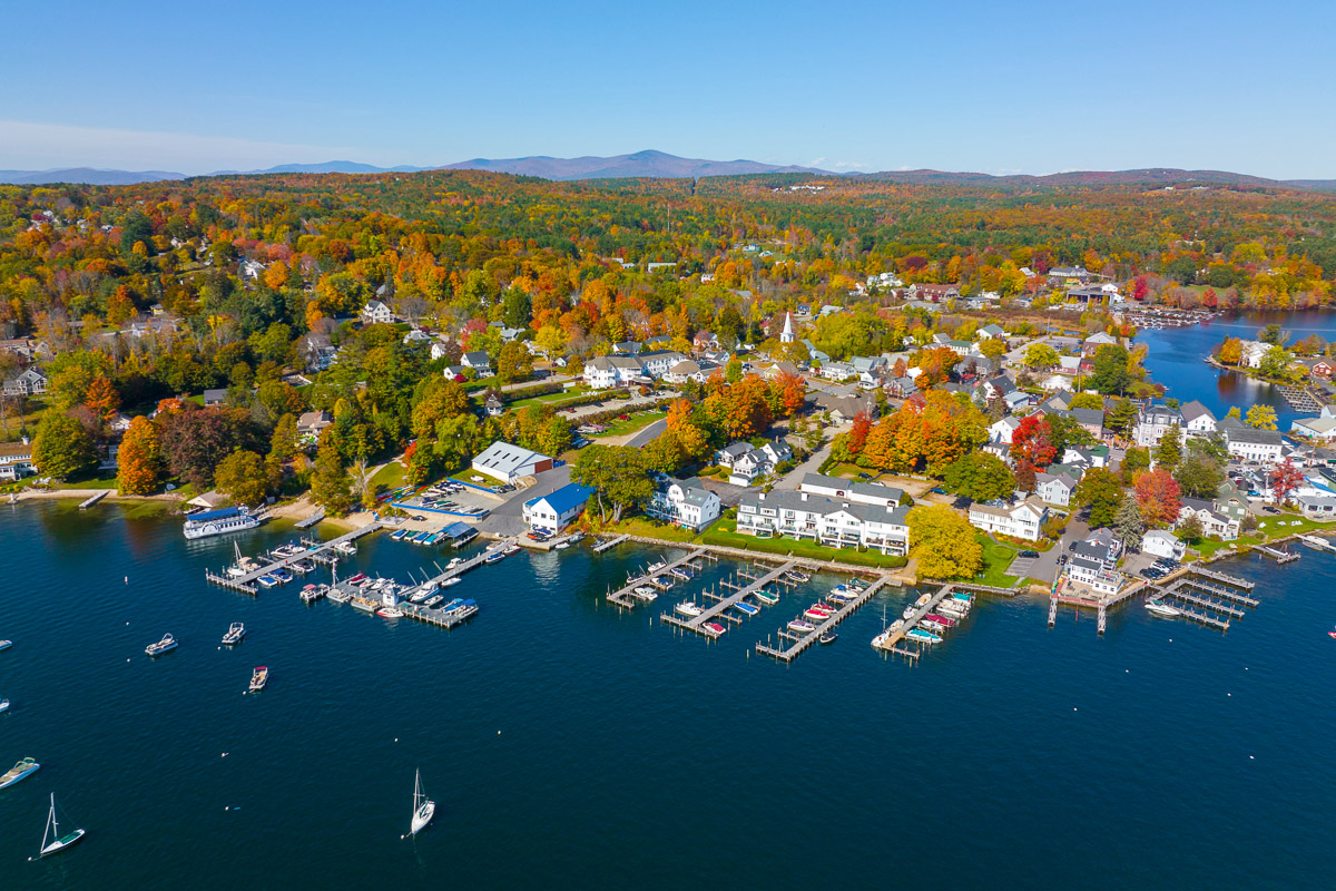 Aerial view of Wolfeboro on Lake Winnipesaukee, New Hampshire, with docks, boats, and vibrant fall foliage across the town.